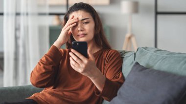 Akıllı telefonundan kötü haberler okuyan bir kadın üzgün ve endişeli.
