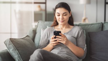 Oturma odasında cep telefonu kullanan bir kadın.