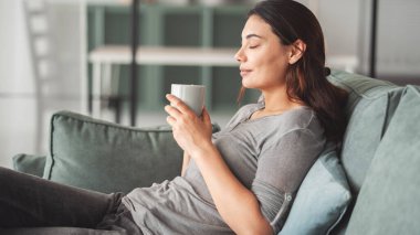 Genç bayan evde kahve içiyor.