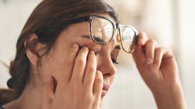 Genç kadın göz ağrısından muzdarip ve gözlerini ovuşturuyor.