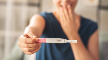 Hamilelik testi yapan bir kadın. Gülümsüyor ve sonuç onu mutlu ediyor.