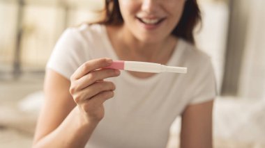 Hamilelik testi yapan bir kadın. Gülümsüyor ve sonuç onu mutlu ediyor.