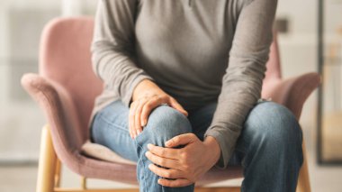 Oturma odasında kanepede oturan kadın diz ağrısı çekiyor.