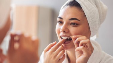 Genç kadın aynanın önünde dişlerini diş ipi