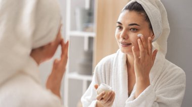 Aynadaki yansıma güzel bir kadın kozmetik cilt bakımı yapıyor.