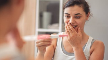 Banyoda hamilelik testi yapan aynalı bir kadının yansıması.