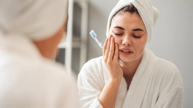 Dişlerini fırçalarken dişi ağrıyan bir kadın.