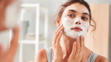 Banyoya yüz maskesi takan genç bir kadın.