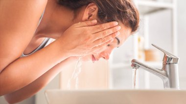 Genç bir kadın banyoda yüzünü yıkıyor.