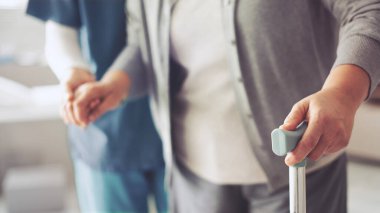 Hemşire yaşlı hastaya bastonla yardım ediyor.