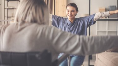 Fizyoterapist yaşlı bir kadının egzersiz yapmasına yardım ediyor.