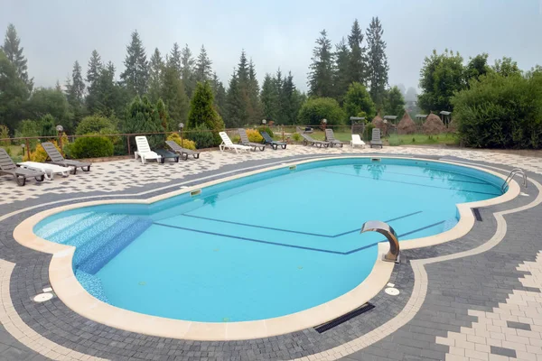 stock image Outdoor swimming pool mountain hotel pool resort chair pool lounge chair relax mountains forest resort. Sunbed mountain resort chaise longue. Blue water forest hotel poolside chairs. No people, nobody