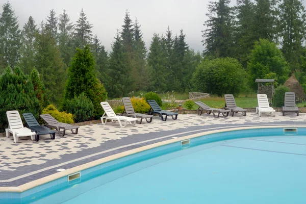 stock image Outdoor swimming pool mountain hotel pool resort chair pool lounge chair relax mountains forest resort. Sunbed mountain resort chaise longue. Blue water forest hotel poolside chairs. No people, nobody