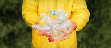 Çevre, parkı temizliyor çöpleri temizliyor. Gönüllü eller plastik çöp şişesini tutuyor. Gönüllü temizleme ormanı. PET atık plastik el çöpleri çöpleri doğayı topluyor. PET plastik kirliliği