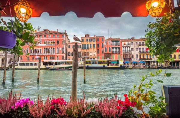 Picturesque view from open cafe with colorful flowers and illumination to Grand Canal and historic buildings. Venice, Italy