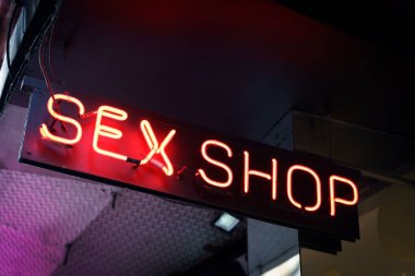 Şehir caddesinde bir seks dükkanının neon işareti. Atmosferik parlayan kırmızı yazı, turist mahallesindeki akşam caddesinde. Yüksek kalite fotoğraf
