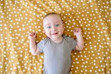 Cheerful baby lies on the bed in the childrens room. Caucasian baby smiles. High quality photo