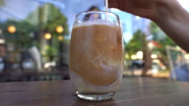 Cold coffee drink in a glass. Girl drinks morning coffee at a table in a cafe. High quality FullHD footage