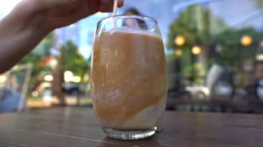 Cold coffee drink in a glass. Girl drinks morning coffee at a table in a cafe. High quality FullHD footage