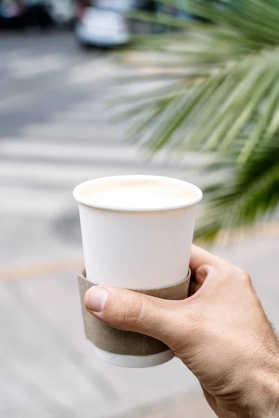 Takeaway coffee in a paper cup. A hand with a drink to go on the background of street. Paper cup mockup. High quality photo