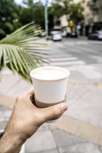 Takeaway coffee in a paper cup. A hand with a drink to go on the background of street. Paper cup mockup. High quality photo