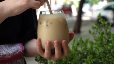 Cold coffee drink in a glass. Girl drinks morning coffee at a table in a cafe. High quality FullHD footage
