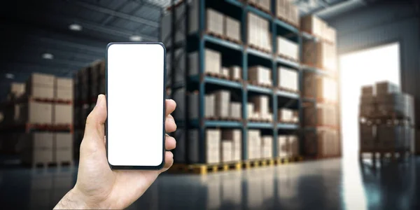 stock image Warehouse with a hand holding an empty smartphone. Blurred industrial warehouse with goods and products. Logistics, business, delivery, services concept. High quality photo