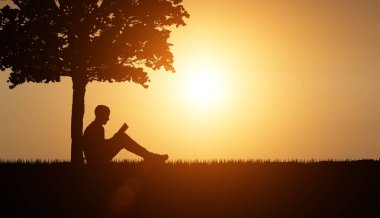 Adam gün batımında doğada bir ağacın altında kitap okuyor. Kitap okuyan bir insanın silueti. Yüksek kaliteli illüstrasyon