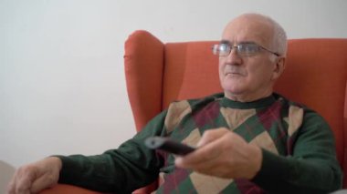 Evde elinde uzaktan kumanda olan yaşlı bir adam. Büyükbabam oturma odasında televizyon izliyor. Yüksek kaliteli FullHD görüntüler