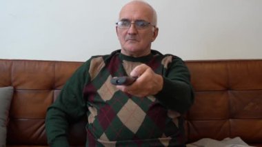 Evde elinde uzaktan kumanda olan yaşlı bir adam. Büyükbabam oturma odasında televizyon izliyor. Yüksek kaliteli FullHD görüntüler