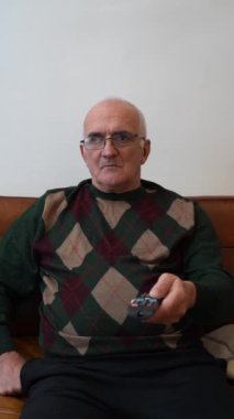 Evde elinde uzaktan kumanda olan yaşlı bir adam. Büyükbabam oturma odasında televizyon izliyor. Yüksek kaliteli FullHD görüntüler