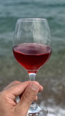 Elinde bir kadeh kırmızı şarap. Deniz sahilinde kırmızı şarap tadımı. Dikey video. Yüksek kaliteli FullHD görüntüler