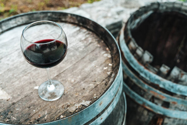 A glass of red wine placed on a weathered oak barrel inside a rustic wine cellar. The image evokes the charm of traditional winemaking, highlighting textures of aged wood and the elegance of fine wine