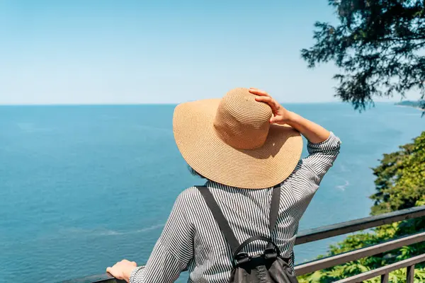 Açık yaz kıyafetleri ve hasır şapkalı genç bir kadın yüksek kıyı manzaralı bir yerde duruyor ve uzak okyanus ufkuna bakıyor. Modern keşiflerin, gezgin şehvetin ve açık havanın özünü yakalıyorum.