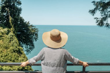 Açık yaz kıyafetleri ve hasır şapkalı genç bir kadın yüksek kıyı manzaralı bir yerde duruyor ve uzak okyanus ufkuna bakıyor. Modern keşiflerin, gezgin şehvetin ve açık havanın özünü yakalıyorum.