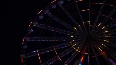 Göz kamaştırıcı neon ışıklarla aydınlatılmış canlı bir dönme dolap gece vakti bir lunaparkta derin siyah gökyüzüne doğru döner. Uzun pozlama hareketi yakalar ve hipnotik dairesel bir etki yaratır.