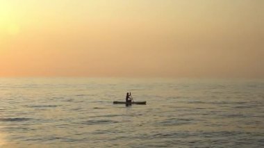 Huzurlu bir yaz günbatımında sakince denizi geçen bir kadının silueti. Altın ışık, suyun üzerinde süzülürken hafif dalgaları yansıtıyor ve huzur yaratıyor.