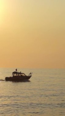 Deniz kurtarma botu dramatik bir akşam günbatımında sakin sularda süzülüyor. Geminin silueti parlayan gökyüzüne karşı duruyor. Uyanıklık, güvenlik ve acil durumu simgeliyor.