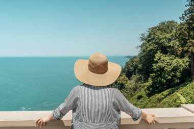 Açık yaz kıyafetleri ve hasır şapkalı genç bir kadın yüksek kıyı manzaralı bir yerde duruyor ve uzak okyanus ufkuna bakıyor. Modern keşiflerin, gezgin şehvetin ve açık havanın özünü yakalıyorum.