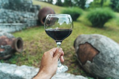 Geleneksel Gürcistan qvevri 'sinin yanında bir bardak kırmızı şarap duruyor. Eski şarap yapımında kullanılan büyük kil kaplar. Kırsal bir ortamda geçen sahne, Gürcistan 'ın zengin mirasını vurguluyor