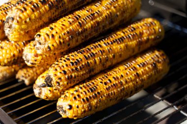 Yakından bakınca altın mısır koçanları açık bir ateşin üzerinde kızartılıyor. Yanmış dokusu ve parlayan kömürleri yaz mevsimini, açık hava yemeklerini ve ağız sulandıran sokak yemekleri geleneklerini anımsatıyor. Mükemmel.