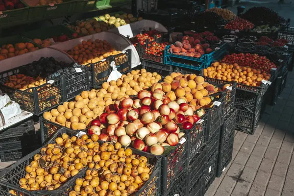 Güneşli bir markette plastik sandıklara yerleştirilmiş renkli taze meyve çeşitleri. Bu canlı yaz sahnesi sokak ticaretinin, sağlıklı beslenmenin ve çiftlikten sofraya geçişin atmosferini yansıtıyor.