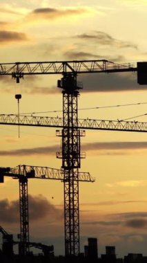 Gün batımında parlayan gökyüzüne çarpıcı bir şekilde kurulmuş inşaat vinçlerinin siluetleri. Bu görsel, kentsel gelişimin, mimari tutkuların ve