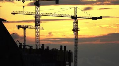 Gün batımında parlayan gökyüzüne çarpıcı bir şekilde kurulmuş inşaat vinçlerinin siluetleri. Bu görsel, kentsel gelişimin, mimari tutkuların ve