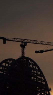 Gün batımında parlayan gökyüzüne çarpıcı bir şekilde kurulmuş inşaat vinçlerinin siluetleri. Bu görsel, kentsel gelişimin, mimari tutkuların ve