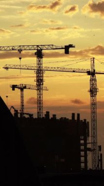 Gün batımında parlayan gökyüzüne çarpıcı bir şekilde kurulmuş inşaat vinçlerinin siluetleri. Bu görsel, kentsel gelişimin, mimari tutkuların ve