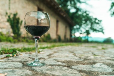 Tek bir kadeh kırmızı şarap, eski bir şarap mahzeninin önünde zarif bir şekilde duruyor. Geleneksel Avrupa şarap imalatının sonsuz cazibesini yakalıyor. Fransa veya İtalya 'da geçen resimde kırsal kesime vurgu yapılıyor