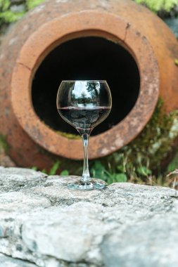 Geleneksel Gürcistan qvevri 'sinin yanında bir bardak kırmızı şarap duruyor. Eski şarap yapımında kullanılan büyük kil kaplar. Kırsal bir ortamda geçen sahne, Gürcistan 'ın zengin mirasını vurguluyor