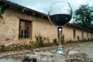 Tek bir kadeh kırmızı şarap, eski bir şarap mahzeninin önünde zarif bir şekilde duruyor. Geleneksel Avrupa şarap imalatının sonsuz cazibesini yakalıyor. Fransa veya İtalya 'da geçen resimde kırsal kesime vurgu yapılıyor