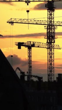 Gün batımında parlayan gökyüzüne çarpıcı bir şekilde kurulmuş inşaat vinçlerinin siluetleri. Bu görsel, kentsel gelişimin, mimari tutkuların ve